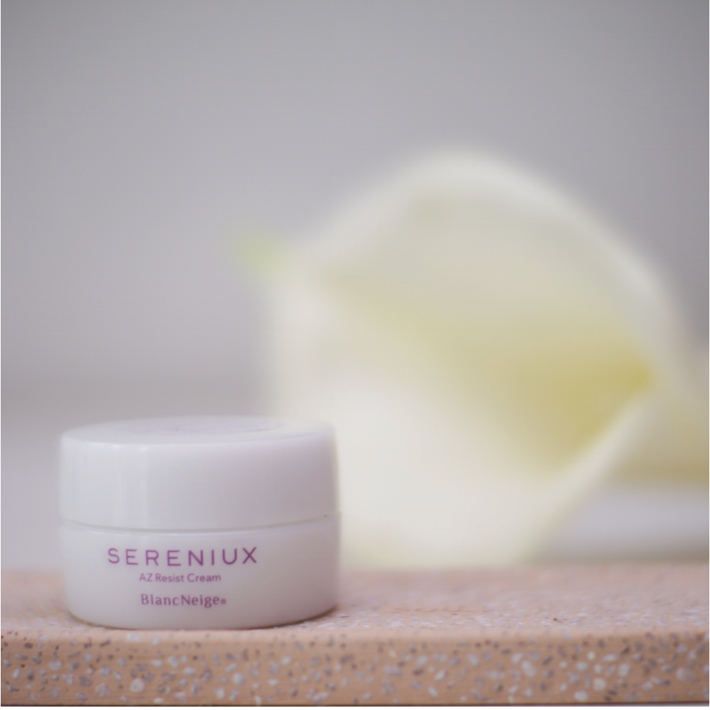 Sereniux anti-aging moisturizer in a white jar on a beach-themed background with a blurred yellow object.